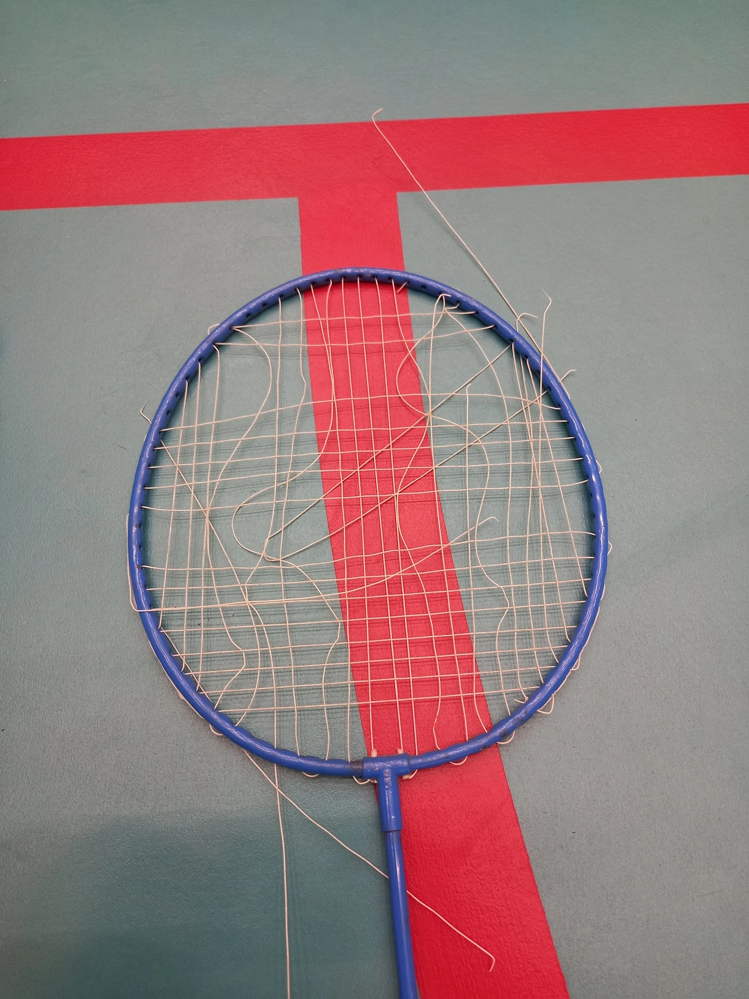 Badmintonracket met blauwe frame en rode grip tegen grijze achtergrond