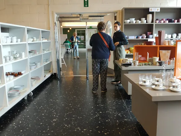 Winkelinterieur met witte stellingen vol serviesgoed, bruine kastjes en twee klanten die rondkijken