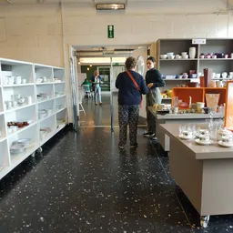 Winkelinterieur met witte stellingen vol serviesgoed, bruine kastjes en twee klanten die rondkijken