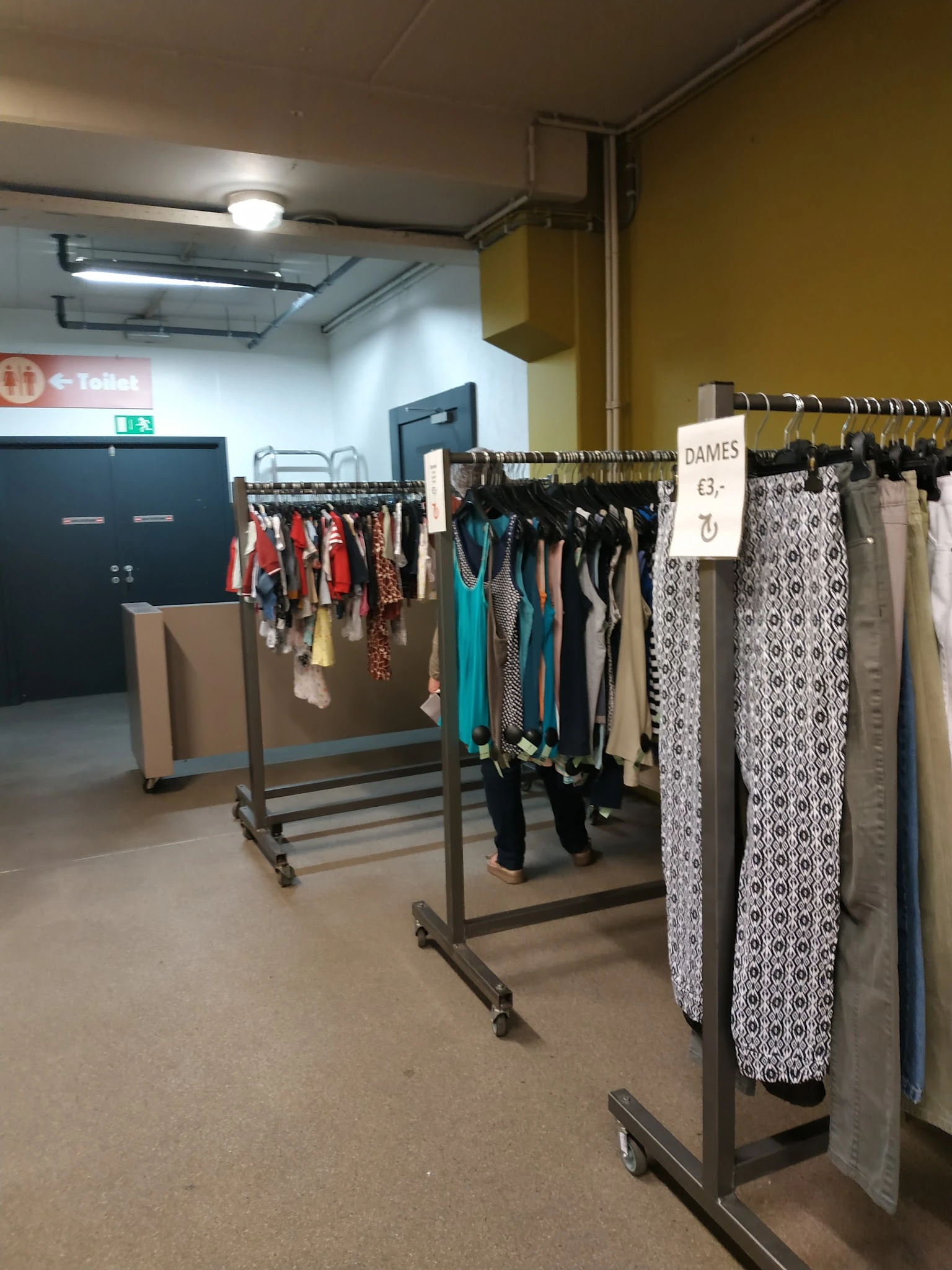 Rekken met tweedehands dameskleding, waaronder jurken, broeken en accessoires in verschillende kleuren en patronen