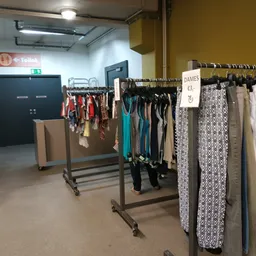 Rekken met tweedehands dameskleding, waaronder jurken, broeken en accessoires in verschillende kleuren en patronen
