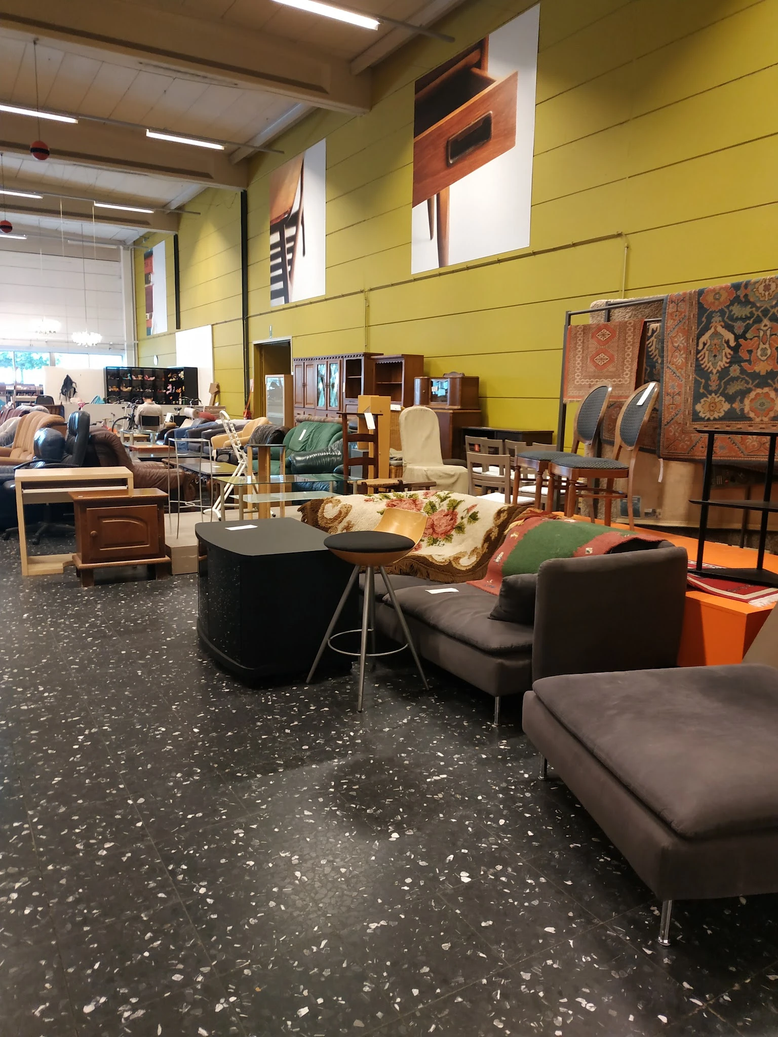 Winkelvloer met diverse meubels: zwarte ronde tafel, bruine fauteuils, houten stoelen, kasten en textiel tegen gele wand
