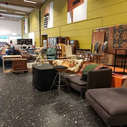Winkelvloer met diverse meubels: zwarte ronde tafel, bruine fauteuils, houten stoelen, kasten en textiel tegen gele wand