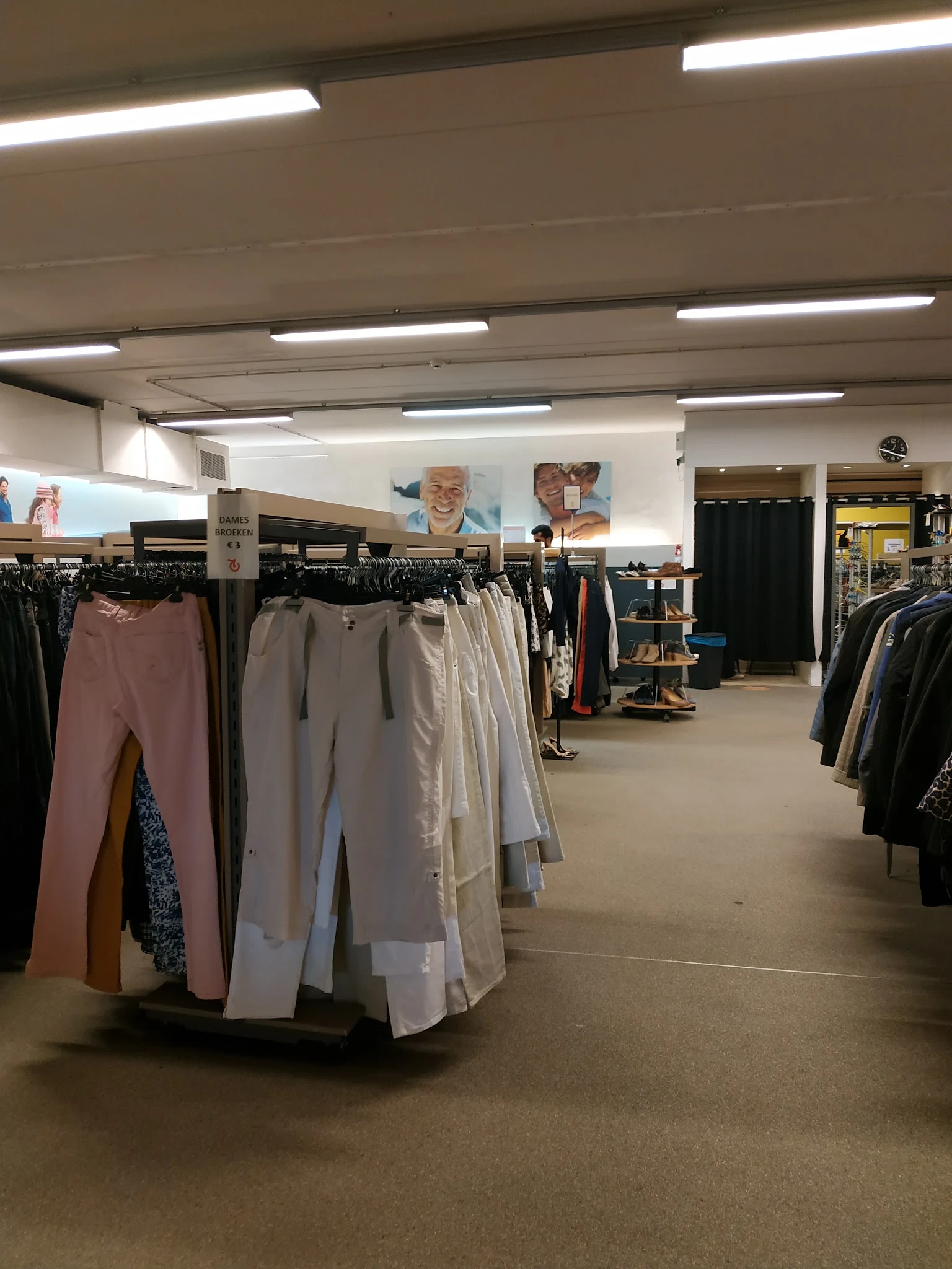 Winkelvloer met kledingrekken met broeken en jasjes, verlicht plafond en winkelafdelingen op de achtergrond