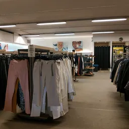 Winkelvloer met kledingrekken met broeken en jasjes, verlicht plafond en winkelafdelingen op de achtergrond