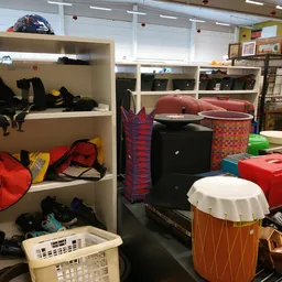 Stellingen met tweedehands spullen: zwarte tassen, rode tas, muziekinstrumenten en diverse opbergboxen in verschillende kleur