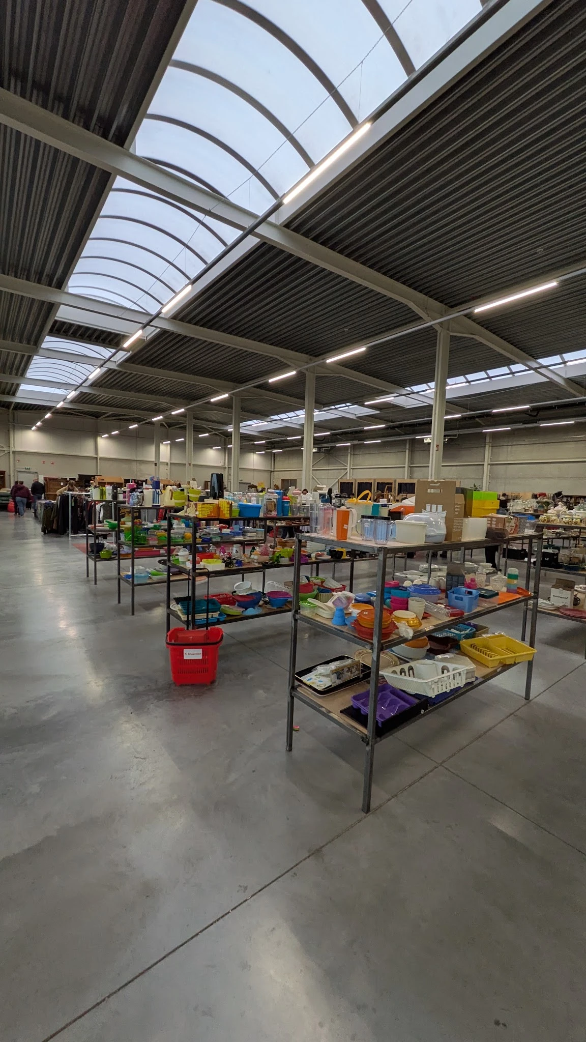 Overzicht van de winkelhal met tafels vol tweedehands spullen, dozen en artikelen onder industriële verlichting