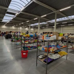 Overzicht van de winkelhal met tafels vol tweedehands spullen, dozen en artikelen onder industriële verlichting
