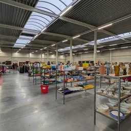 Ruim magazijn met metalen stellingen vol tweedehands artikelen, onder daglichtdaken