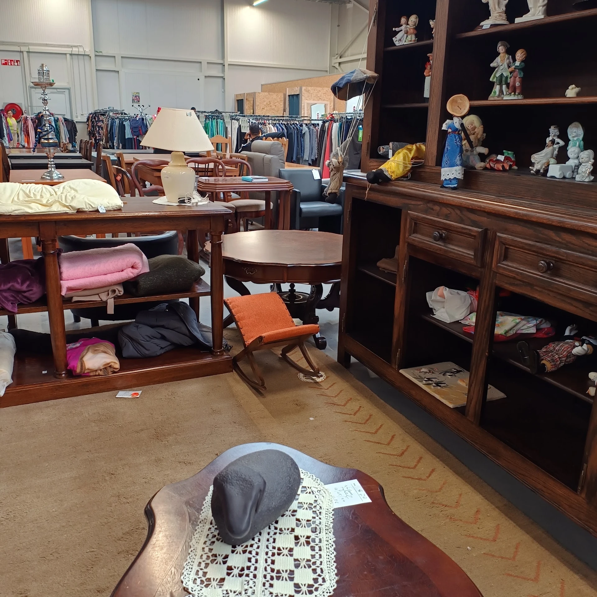 Winkelvloer met houten meubels, kleding op hangers en diverse artikelen in een kringloopwinkel
