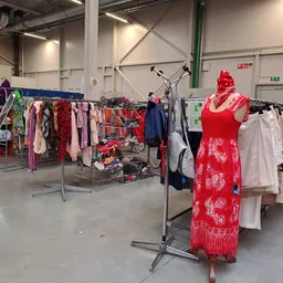 Rekken met tweedehands kleding in verschillende kleuren en stijlen, waaronder een rode jurk op een etalagepop