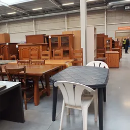 Uitgestalde houten meubels in een kringloopwinkel: tafels, stoelen en kasten