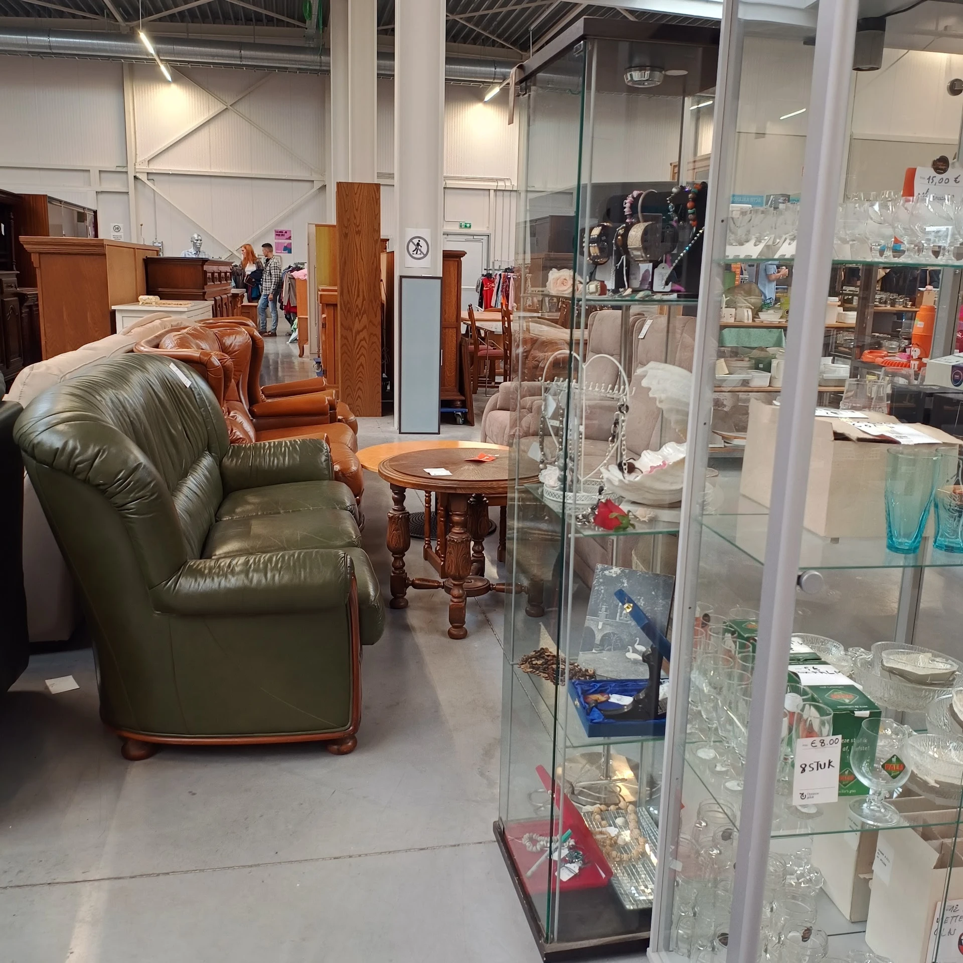 Winkelvloer met groene lederen fauteuil, houten tafeltje en glazen vitrinekasten met diverse items