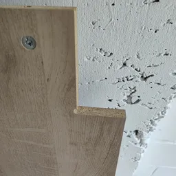 Hoekdetail van houten vloer met witte plafond met gaatjes