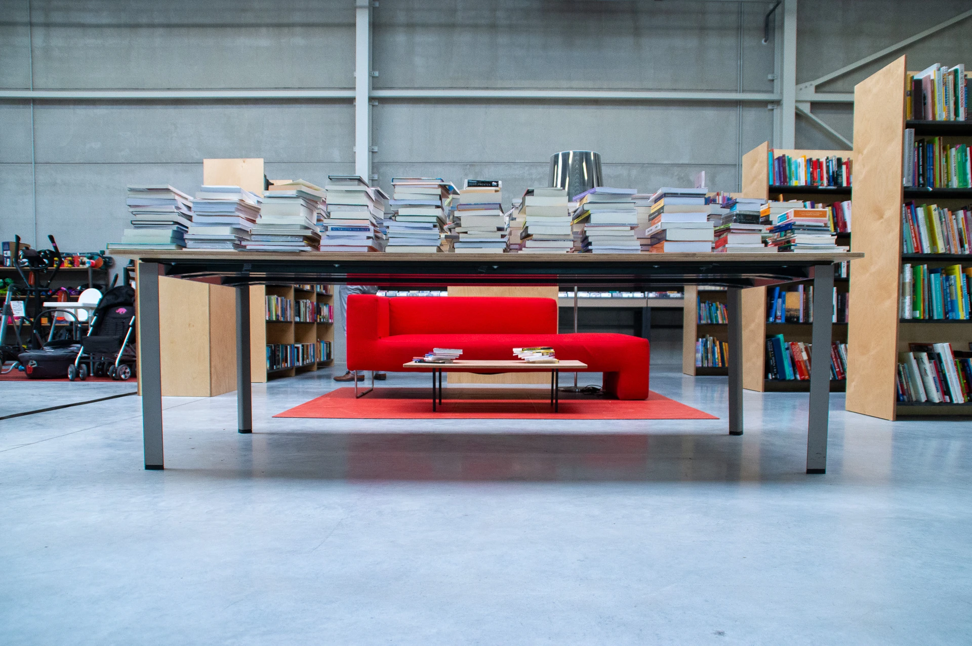 Ruime winkelruimte met grote tafel met boeken, rode bank op rood tapijt en houten boekenkasten
