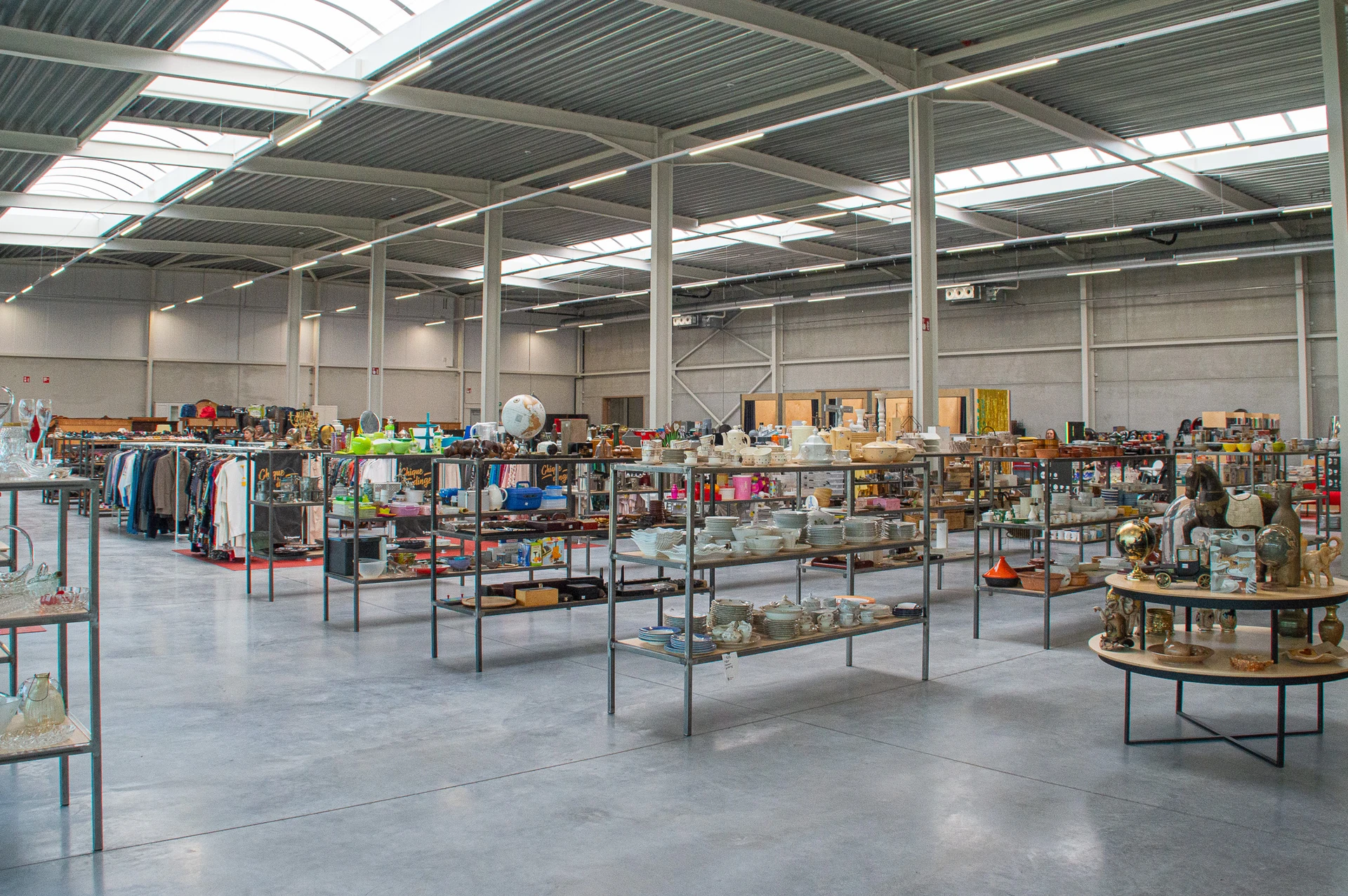 Ruime kringloopwinkel met verschillende afdelingen, tafels met huishoudwaren, kleding en diversen artikel