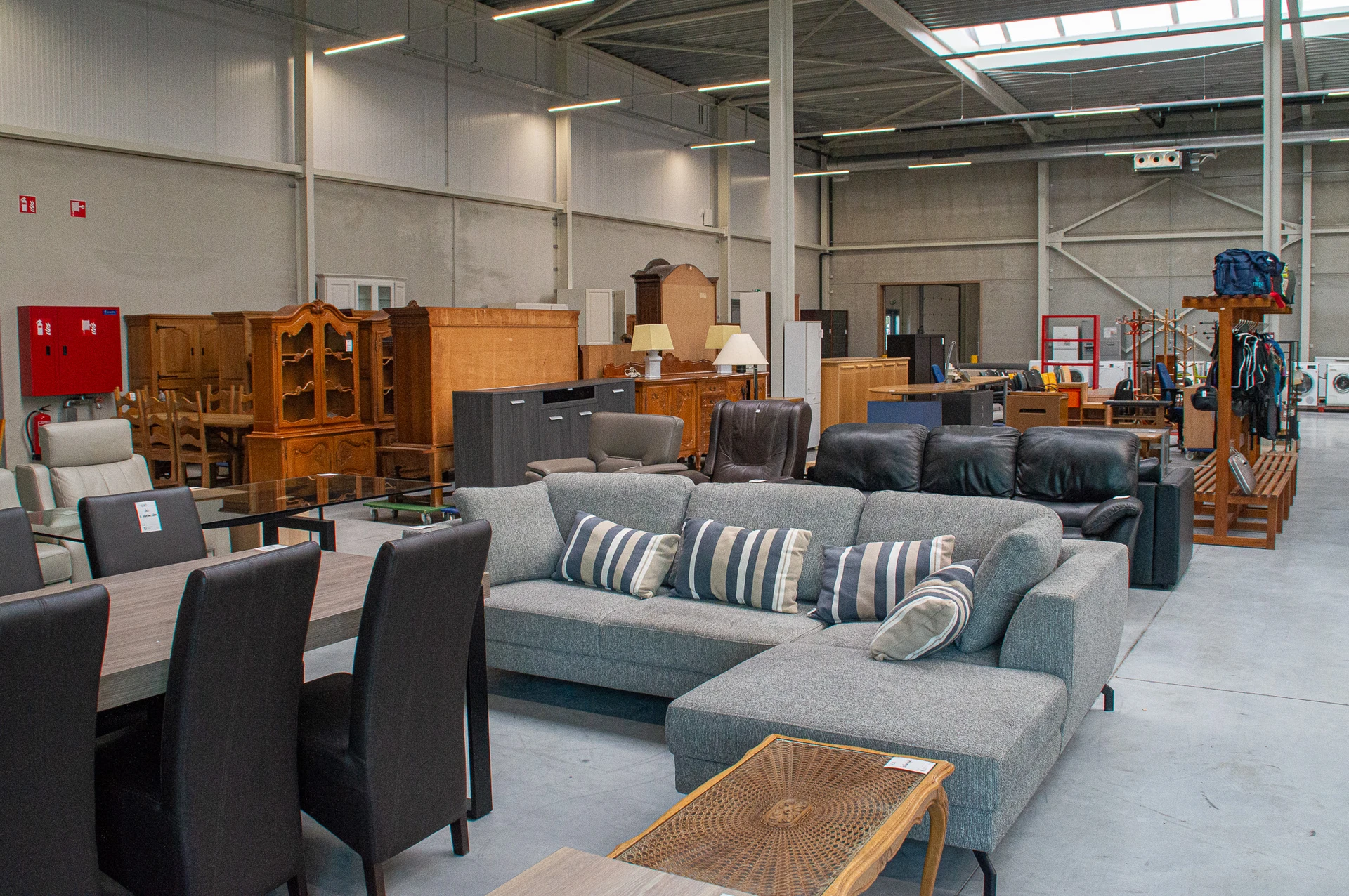 Grijze hoekbank met kussens en houten meubels in een kringloopwinkel
