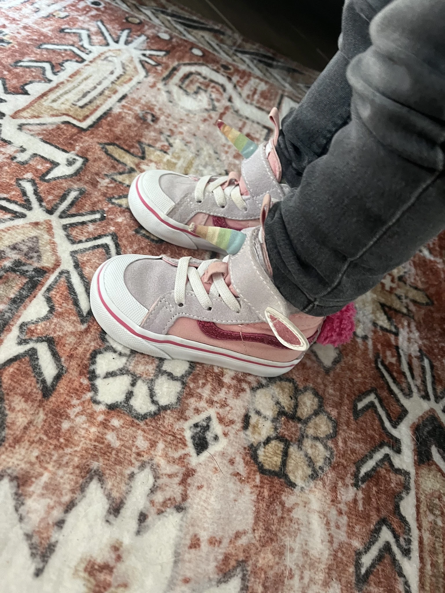 Paar kinderschoenen in grijs en roze met witte zool, gedragen door kind op gebloemd tapijt