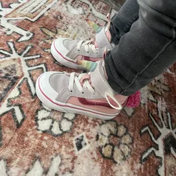 Paar kinderschoenen in grijs en roze met witte zool, gedragen door kind op gebloemd tapijt