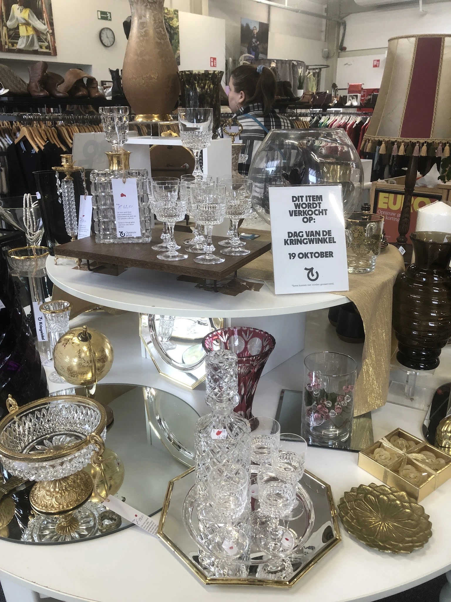 Uitgestalde kristallen glazen en vazen op witte ronde tafels in de winkel