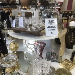 Uitgestalde kristallen glazen en vazen op witte ronde tafels in de winkel