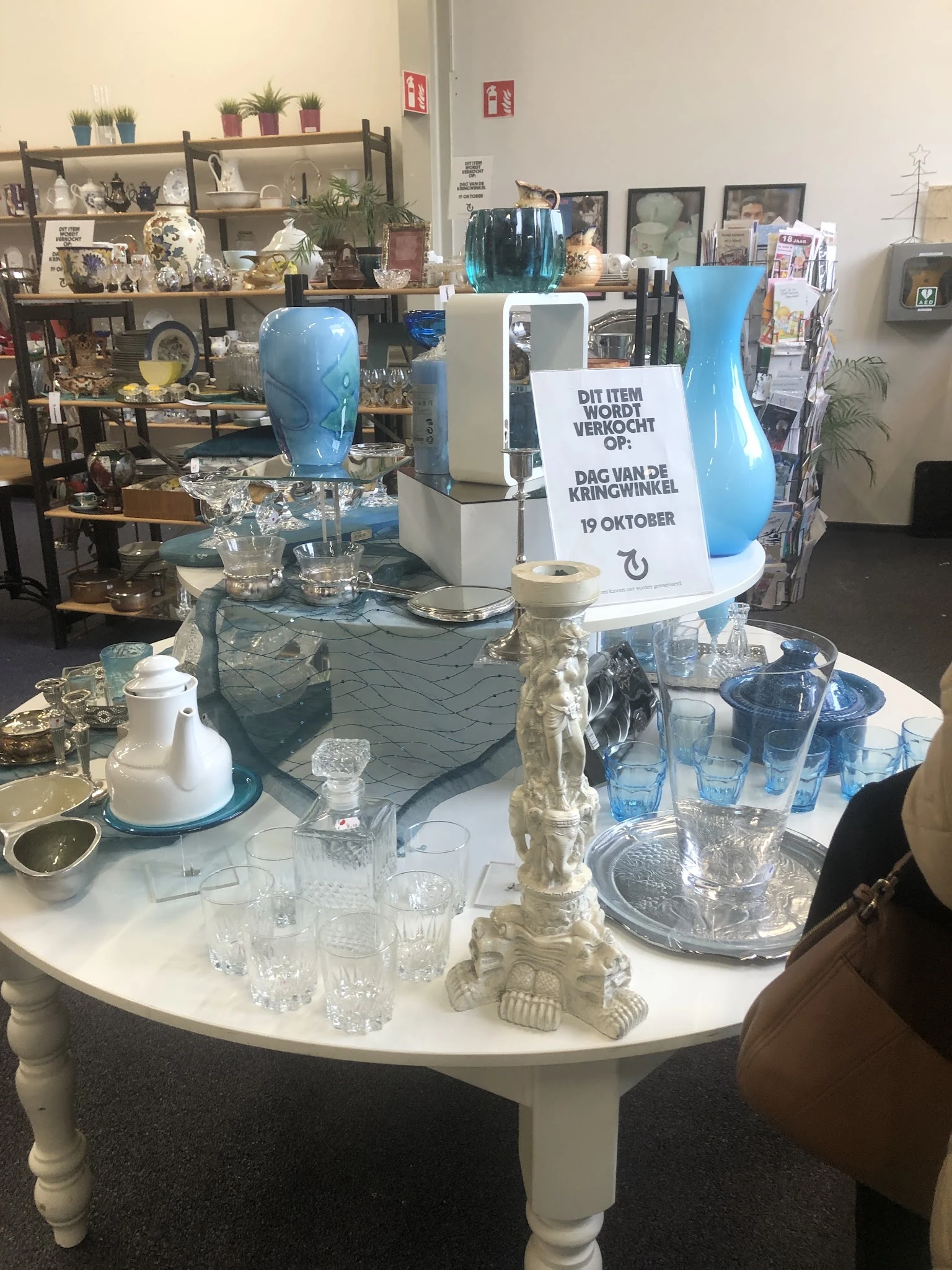 Uitstalling van huisraad en decoratieve items op tafels: blauwe vazen, glazen, servies en andere gebruiksartikelen.