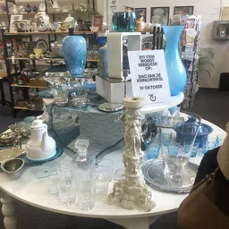 Uitstalling van huisraad en decoratieve items op tafels: blauwe vazen, glazen, servies en andere gebruiksartikelen.