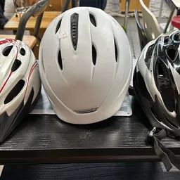 Drie fietshelmen in verschillende kleuren (wit met rood, wit, zwart-wit) uitgestald op een zwarte plank