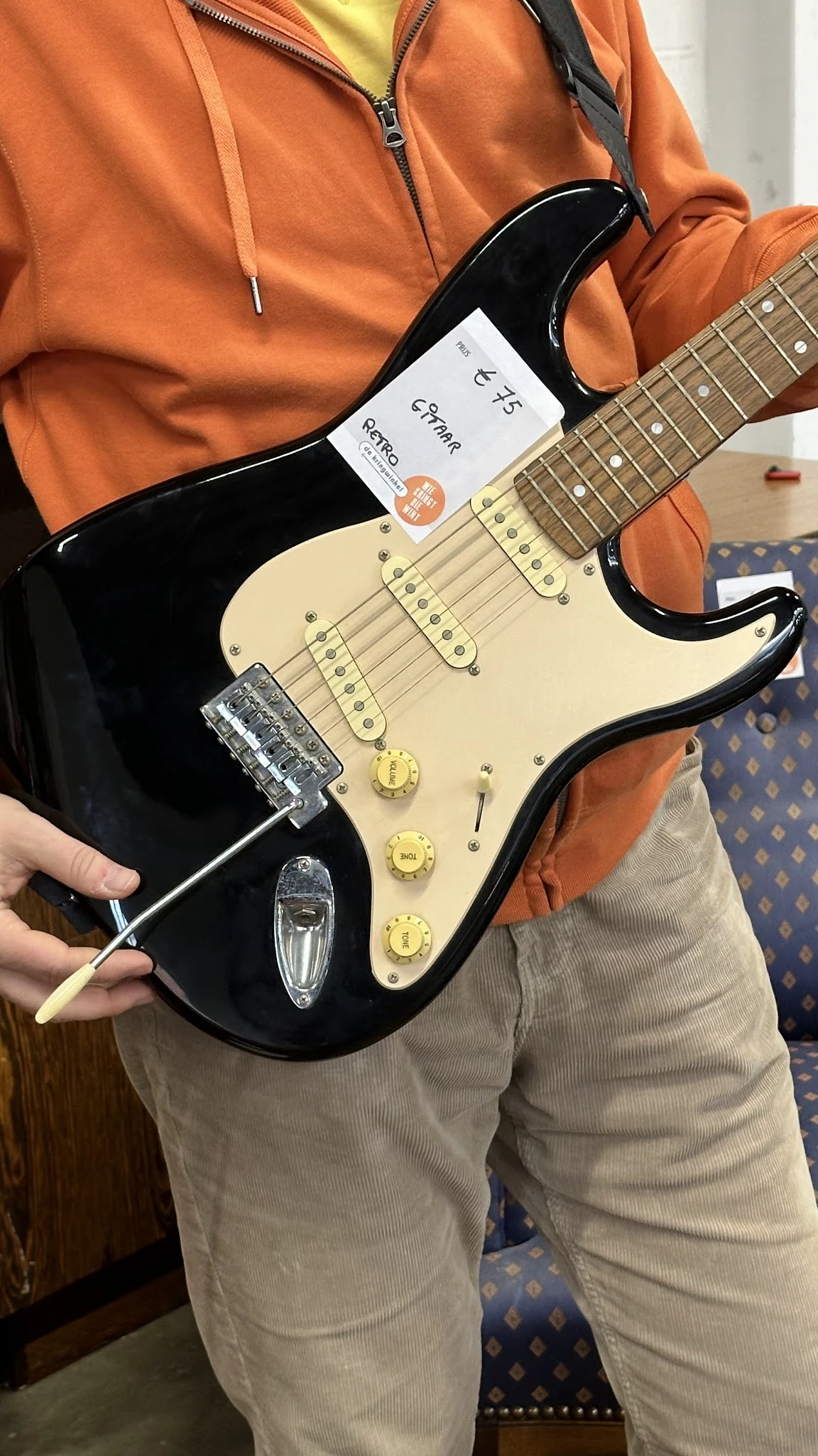 Close-up van een zwarte elektrische gitaar met crèmekleurig pickguard en gouden controls