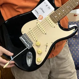 Close-up van een zwarte elektrische gitaar met crèmekleurig pickguard en gouden controls