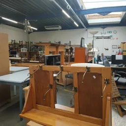 Overzicht van de winkelruimte met houten kasten, meubels en werkstations, bezoekers zichtbaar op de achtergrond