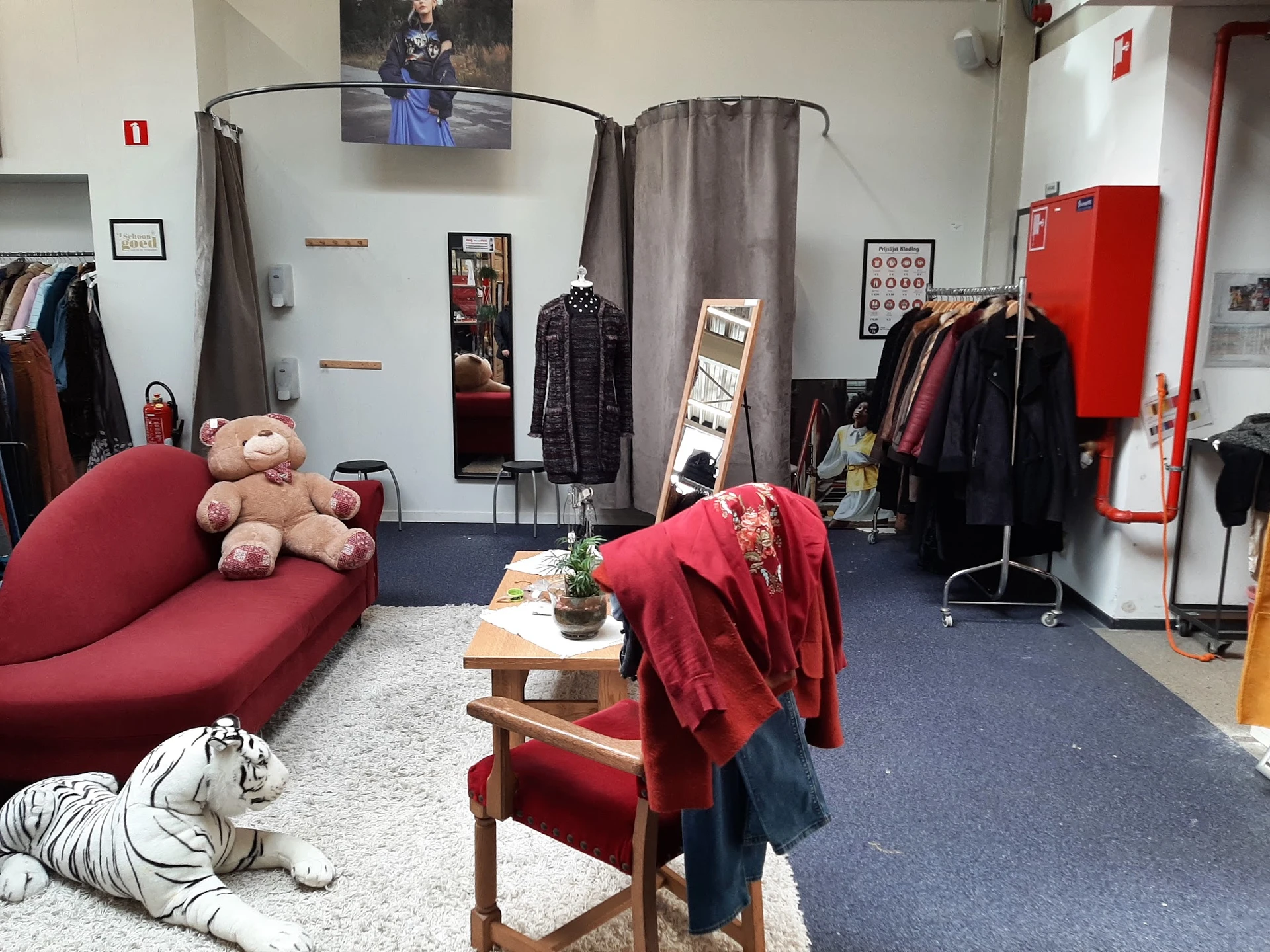 Winkelvloer met kledingrekken, rode bank met knuffels en houten tafel met rode kleding erop