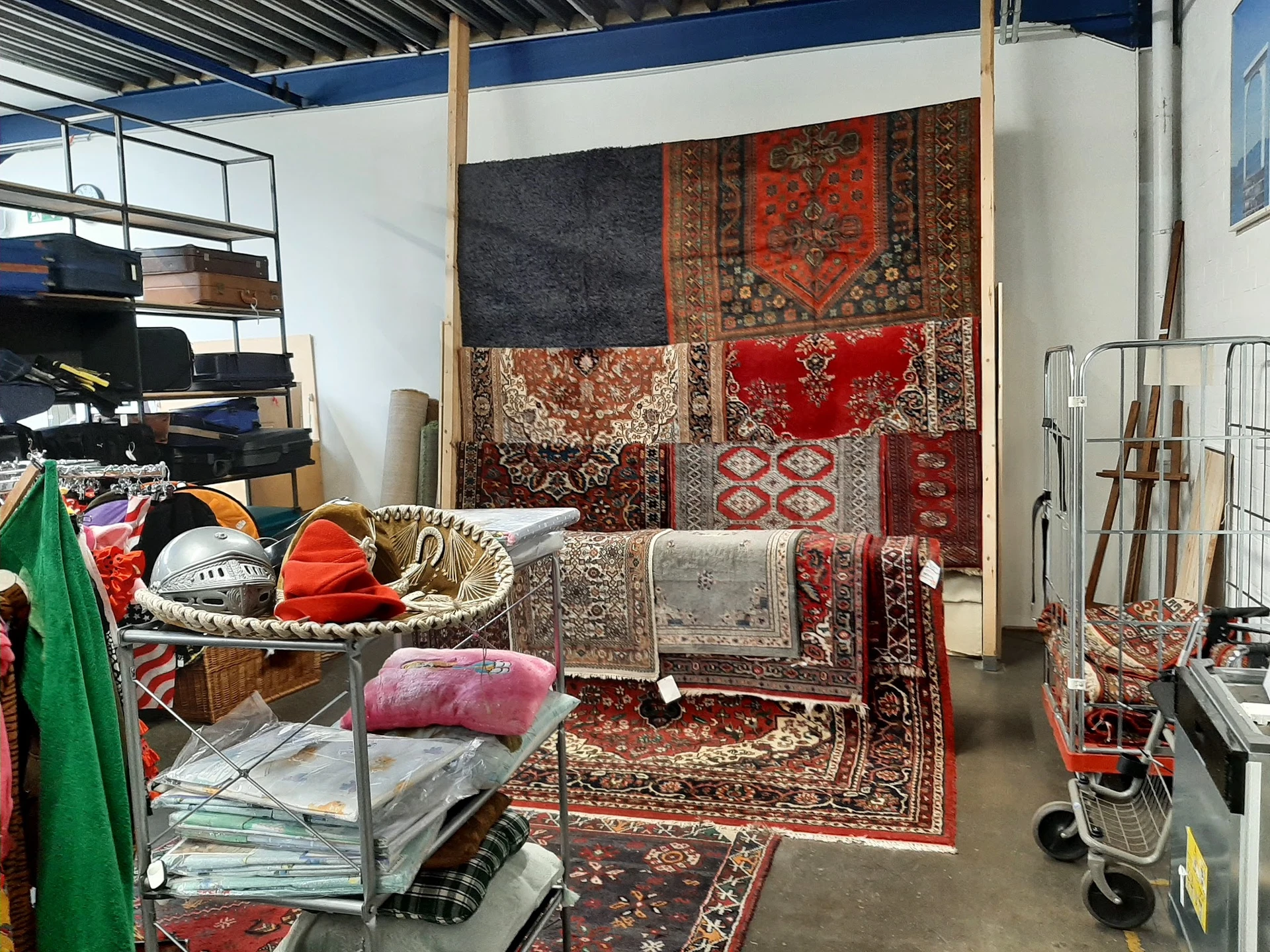Uitgestalde tweedehands tapijten, vloerkleden en huishoudelijke artikelen in een kringloopwinkel