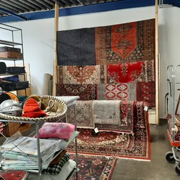 Uitgestalde tweedehands tapijten, vloerkleden en huishoudelijke artikelen in een kringloopwinkel