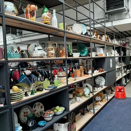 Metalen stellingen met diverse tweedehands huishoudartikelen, servies, decoratie en gebruiksvoorwerpen