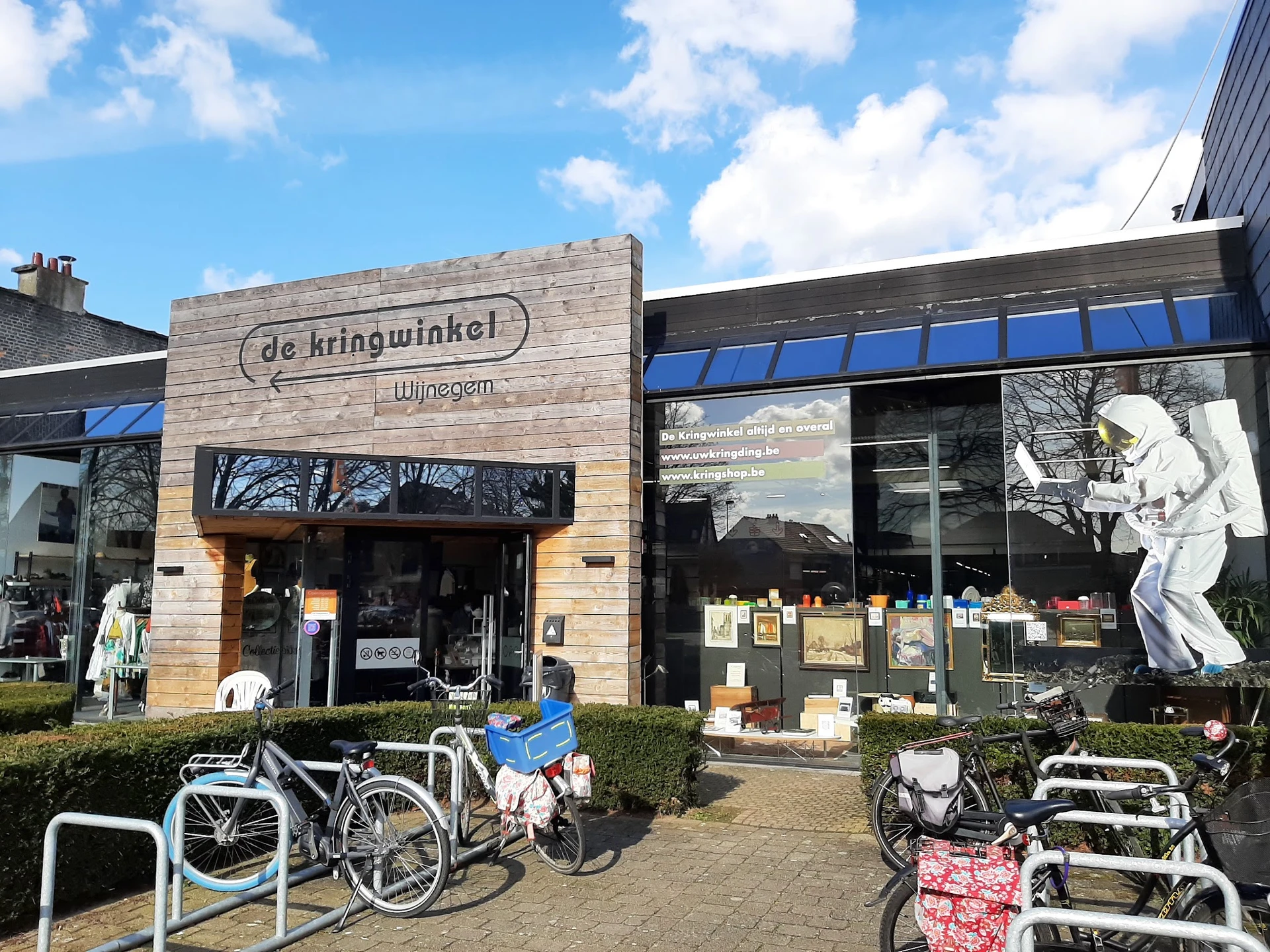 Houten gevel van kringloopwinkel met naam, grote ramen, fietsen voor de ingang