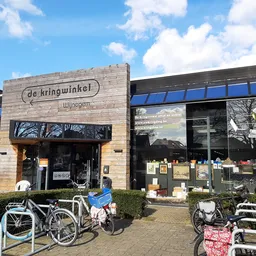 Houten gevel van kringloopwinkel met naam, grote ramen, fietsen voor de ingang