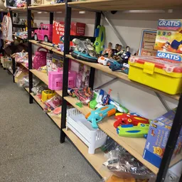 Stellingen met speelgoed en kinderspullen, waaronder roze poppen, auto's, puzzels en andere kinderspeelgoed