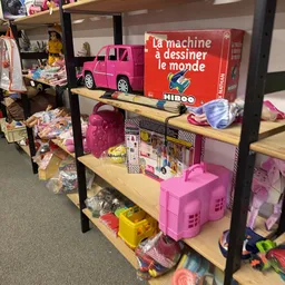 Stellingen met tweedehands speelgoed en kinderspeelgoed, waaronder roze auto's, poppen en huisjes
