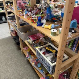 Houten stellingkast met plastic bakken vol speelgoed, poppen en kinderartikelen