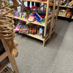 Houten stellingkast met verschillende speelgoed en kinderspullen op verschillende niveaus in een kringloopwinkel