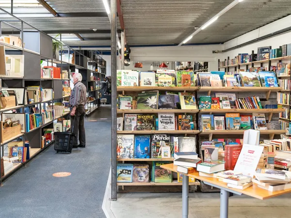 Boekenrekken met tweedehands boeken in een kringloopwinkel, klant aan het bladeren