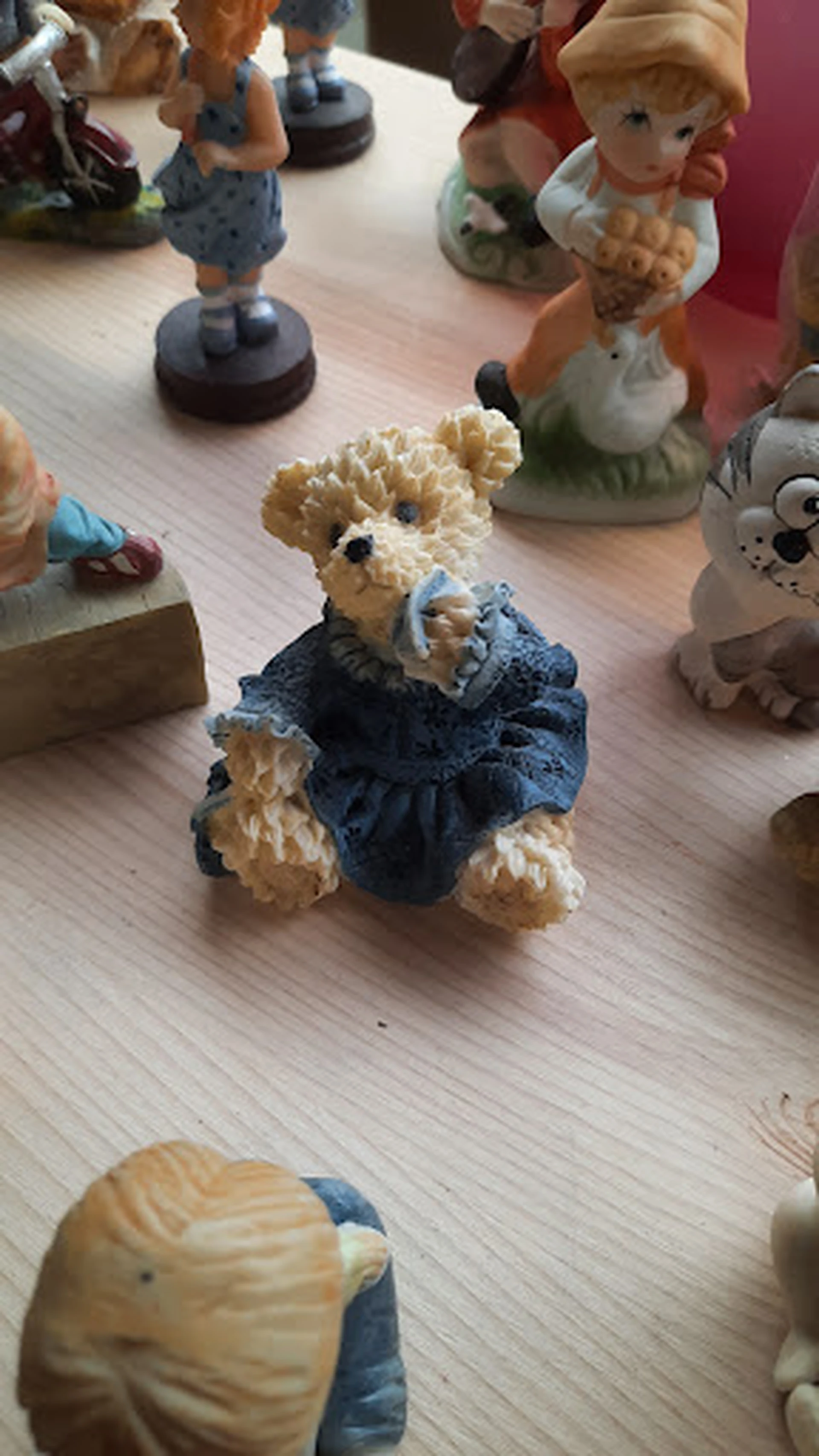Knuffelbeer van beige pluche in blauw jurkje met strik, staand op houten vloer.