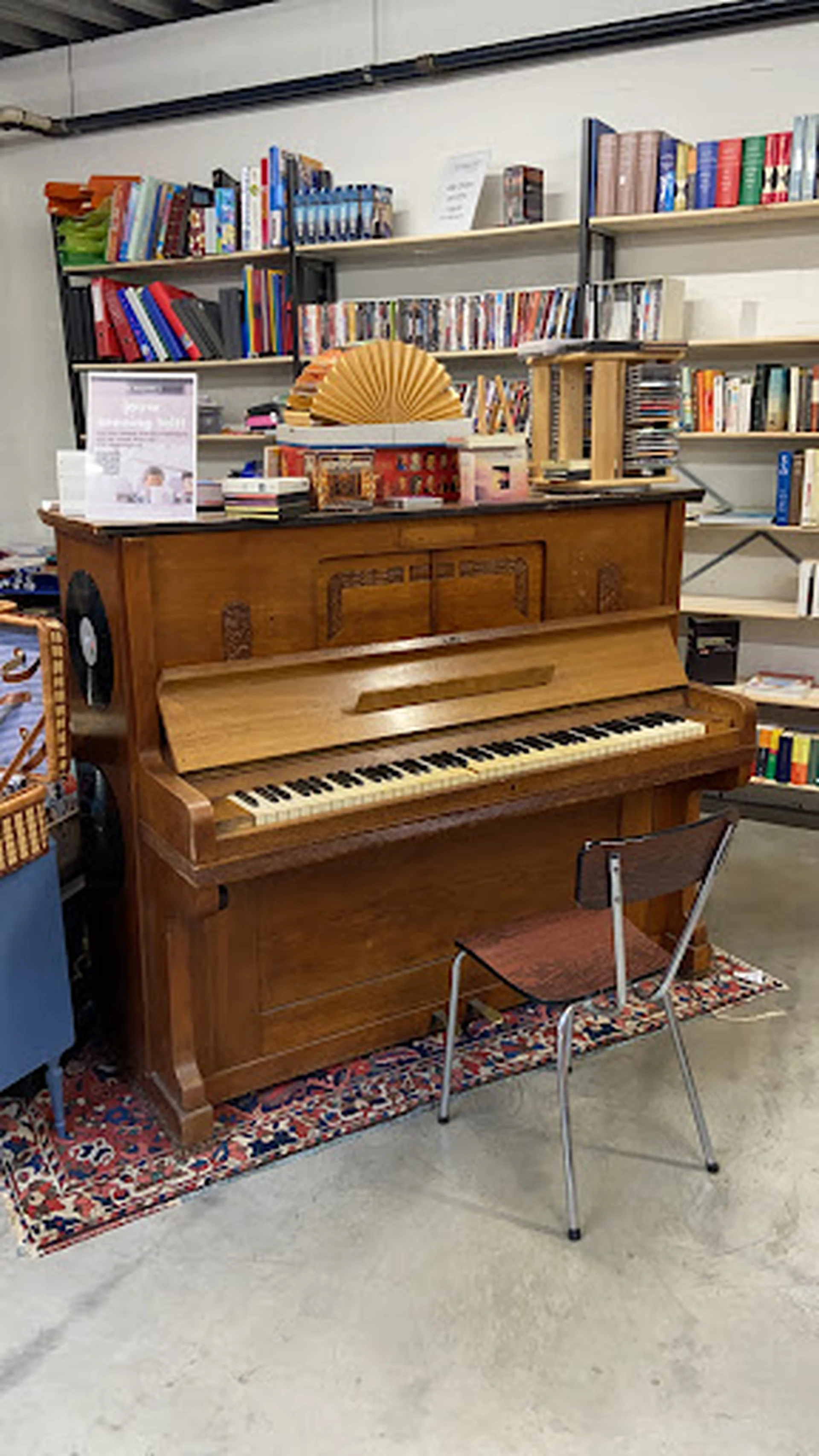 Houten piano in bruine kleur met open klep, staande in een winkelinterieur met boekenkasten op de achtergrond