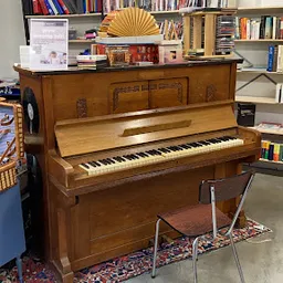 Houten piano in bruine kleur met open klep, staande in een winkelinterieur met boekenkasten op de achtergrond