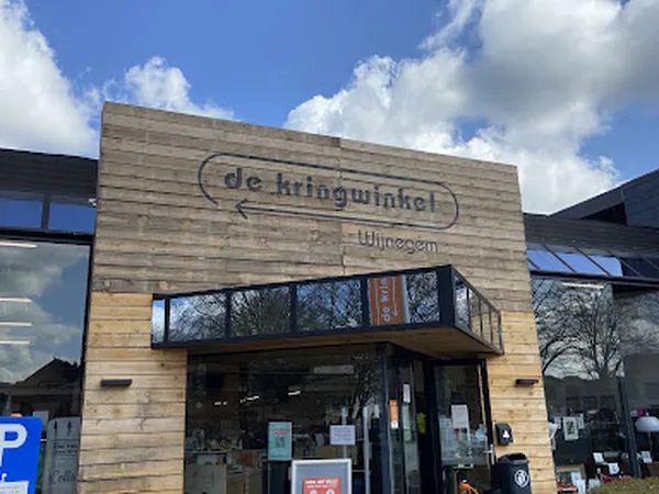 Houten gevel van kringloopwinkel met bord 'de kringwinkel' en naam 'Wijnegem', parkeerplaats zichtbaar
