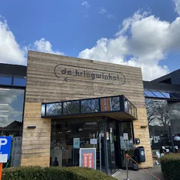Houten gevel van kringloopwinkel met bord 'de kringwinkel' en naam 'Wijnegem', parkeerplaats zichtbaar