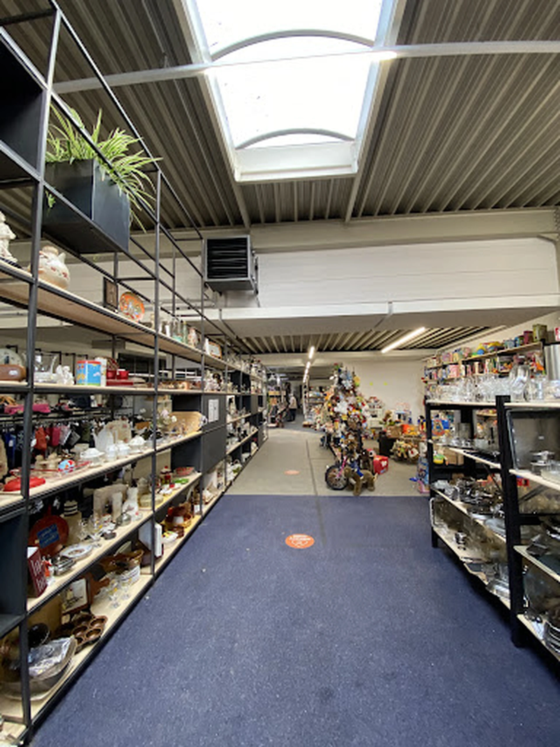 Winkelgang met stellingen vol spullen aan beide zijden, overzicht van het aanbod in de kringloopwinkel