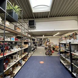 Winkelgang met stellingen vol spullen aan beide zijden, overzicht van het aanbod in de kringloopwinkel