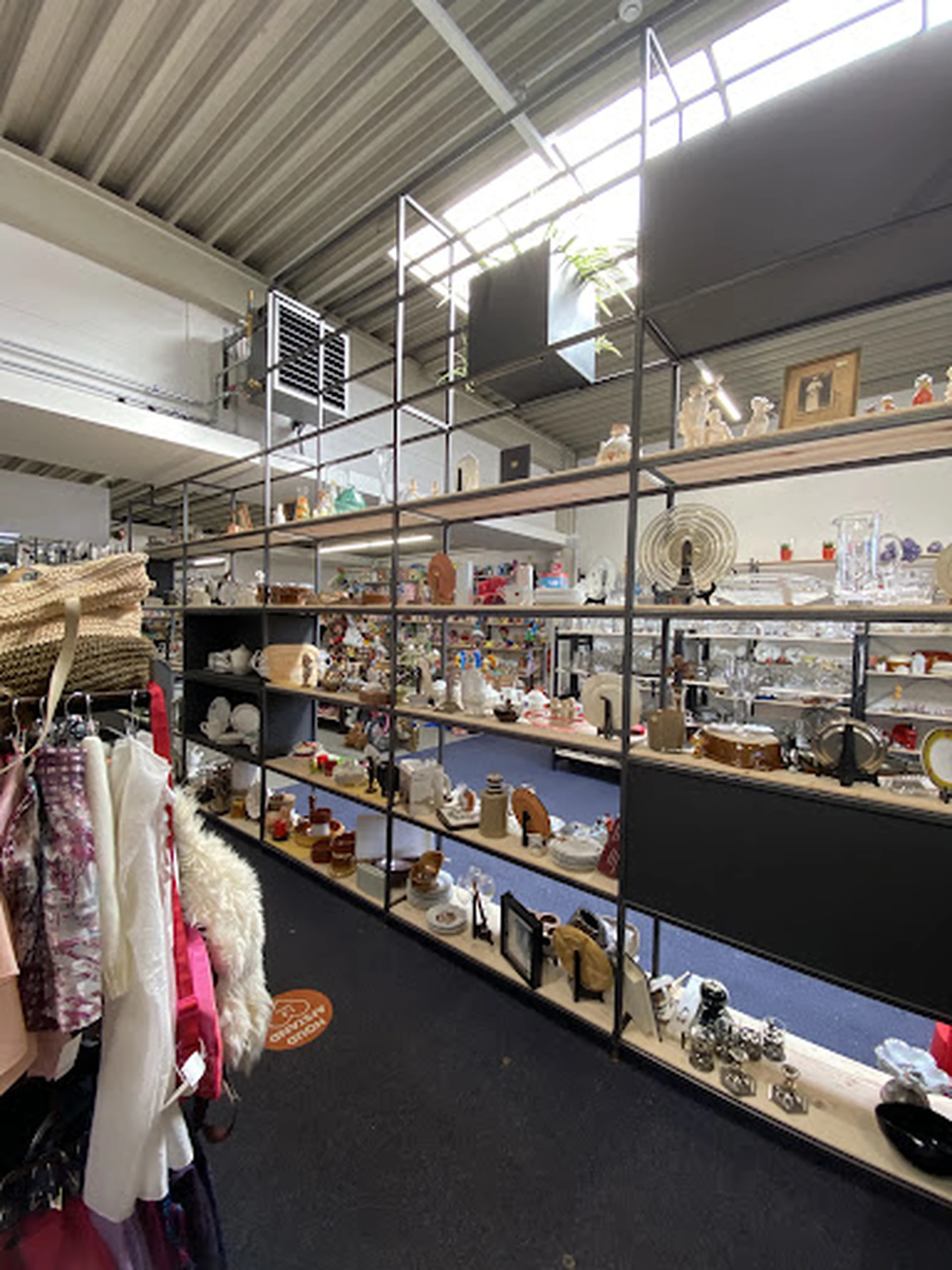 Verschillende tweedehands decoratieartikelen, servies en huishoudspullen uitgestald op metalen stellingen